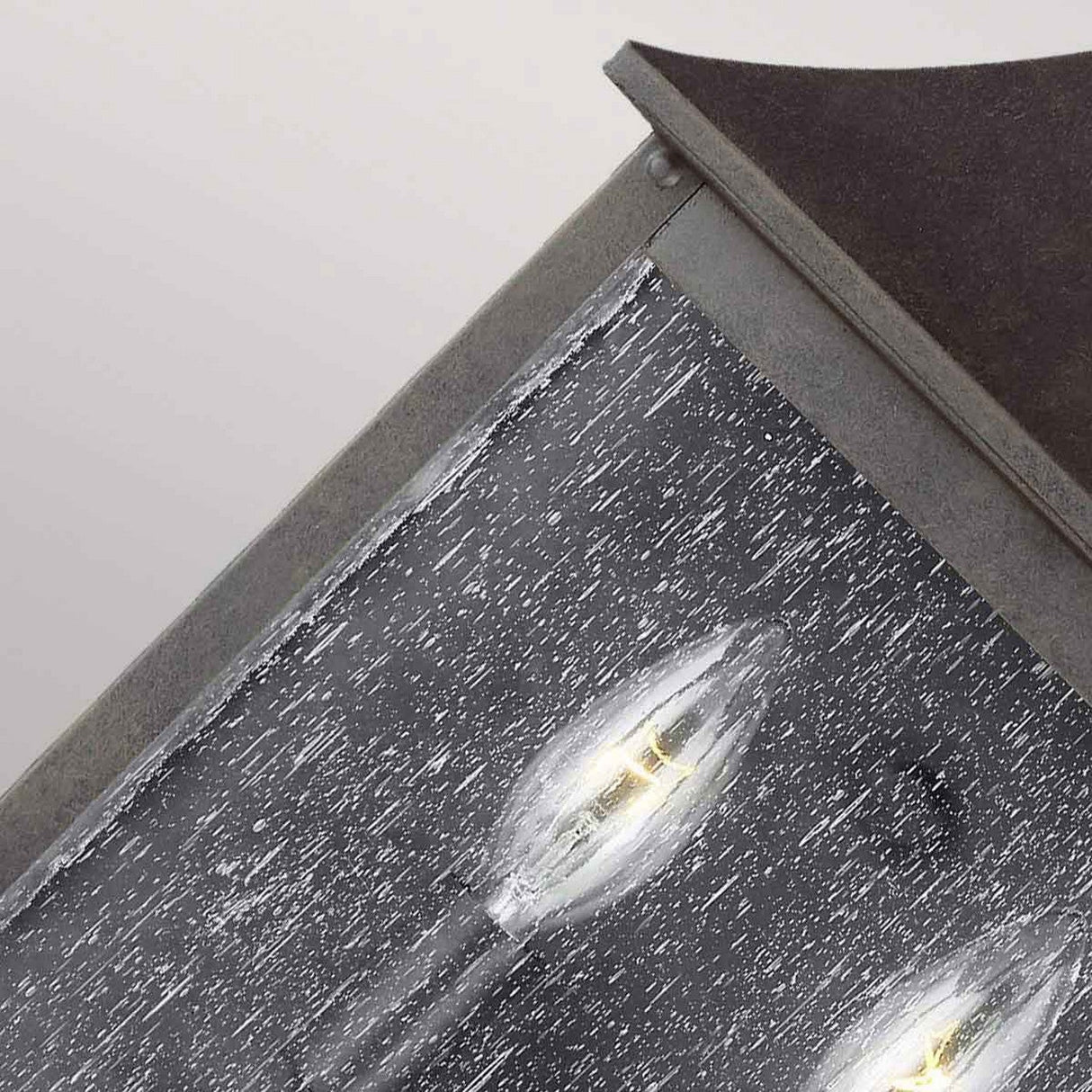 Close-up view of the weathered, rustic Galena 2 Light Outdoor Half Lantern in Grey, featuring a metal frame with multiple candle-like LED bulbs. The seeded glass of this exterior lighting shows signs of wear, enhancing its vintage or aged appearance.
