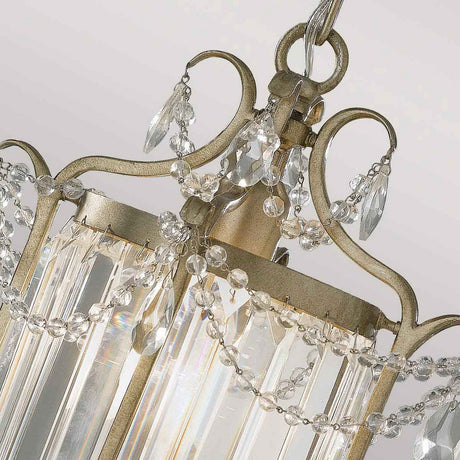 The Gianna 1 Light Pendant in Gilded Silver showcases a close-up of its intricate design with crystal embellishments and beads, exuding timeless elegance. Its metal frame, featuring a vintage distressed gold-like finish, harmonizes beautifully with the crystals that reflect light to create a stunning sparkling effect against a beige background.