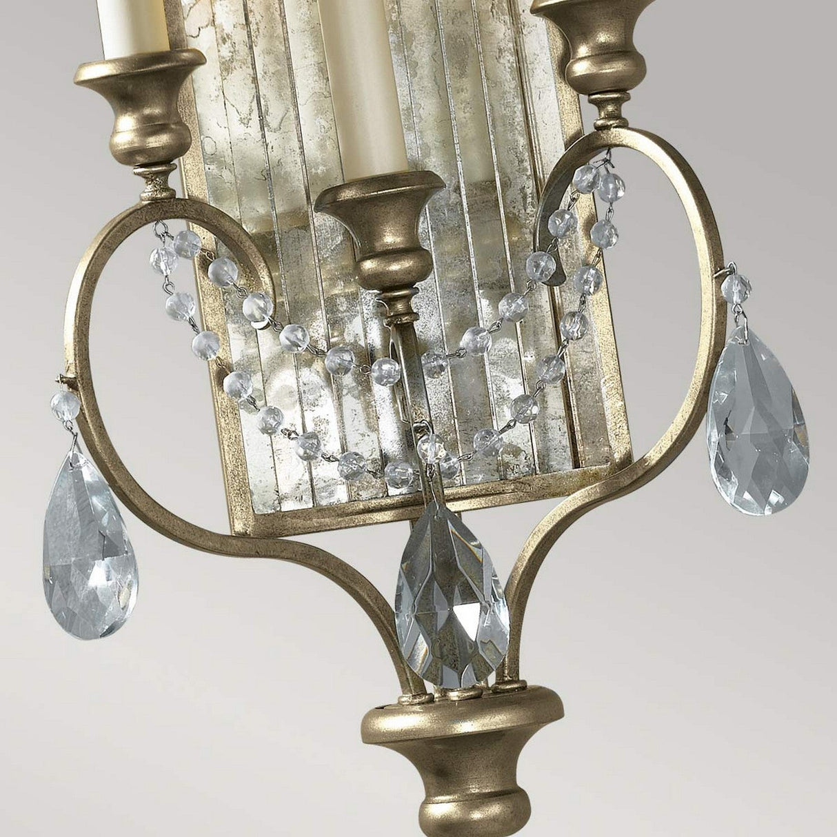 A close-up of a decorative gilded silver sconce adorned with hand-cut crystal drops and bead garlands. Two candle-like lights grace the sconce, reminiscent of the elegant Gianna 3 Light Wall Light - Gilded Silver, positioned against a reflective background.