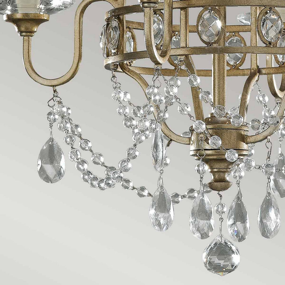 Close-up of the sophisticated Gianna 4 Light Chandelier - Gilded Silver, an Italian design masterpiece showcasing intricate metalwork. This chandelier is adorned with hand-cut crystal embellishments and teardrop-shaped pendants, beautifully reflecting light to create a sparkling effect against a neutral background.