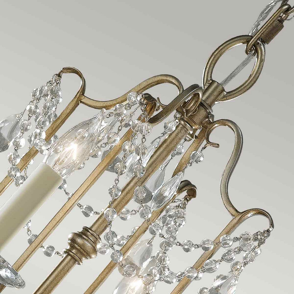 Close-up of the Gianna 4 Light Chandelier - Gilded Silver, an Italian design masterpiece featuring hand-cut crystal embellishments. Its ornate gilded silver metal frame houses four candle-like bulbs, elegantly arranged with decorative metal and crystal elements for a luxurious and classic appearance.