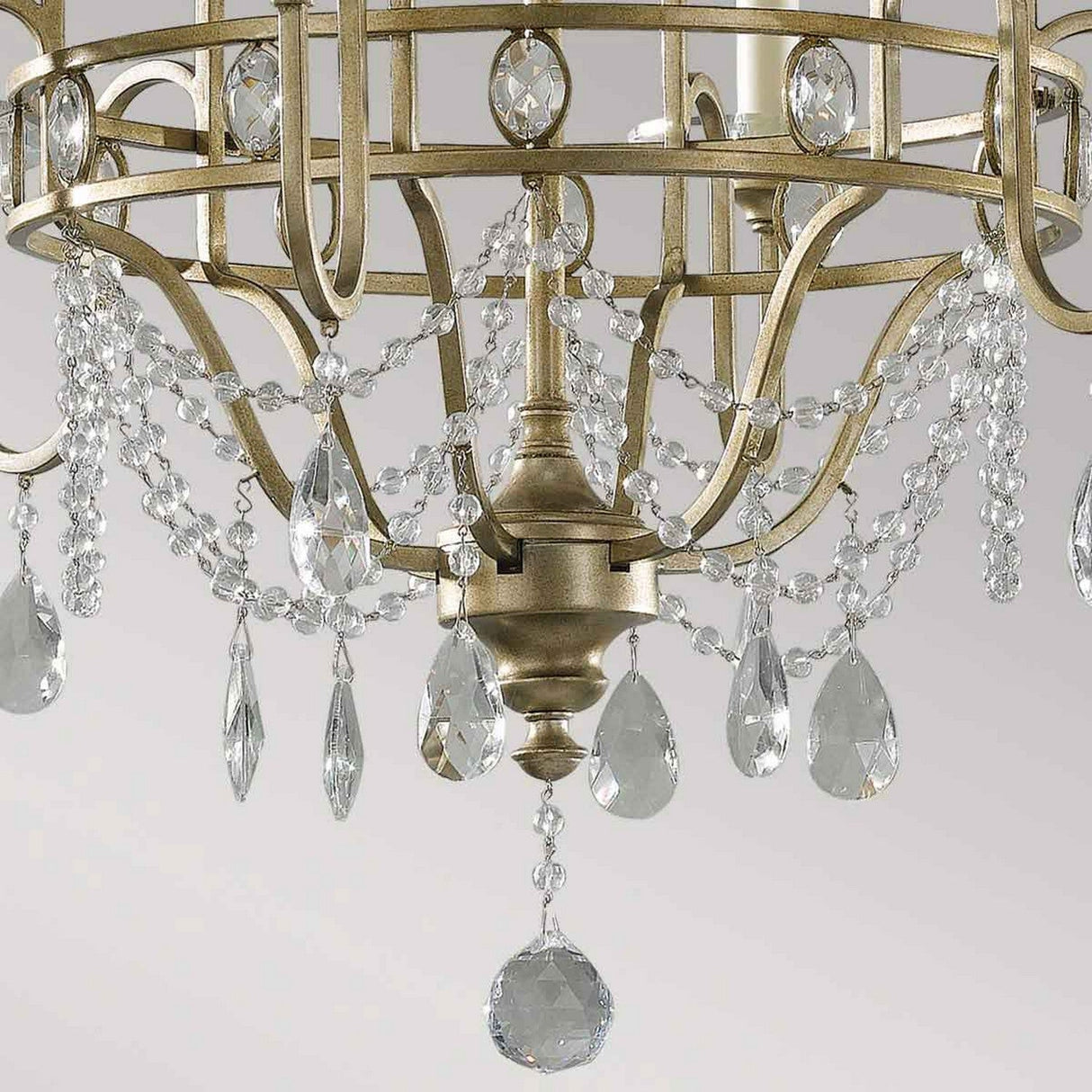 Close-up of the Gianna 6 Light Chandelier - Gilded Silver, showcasing a gilded silver metal frame adorned with hand-cut crystals. The chains of crystals reflect light beautifully, adding elegance to the design. The background is a plain, soft gray.