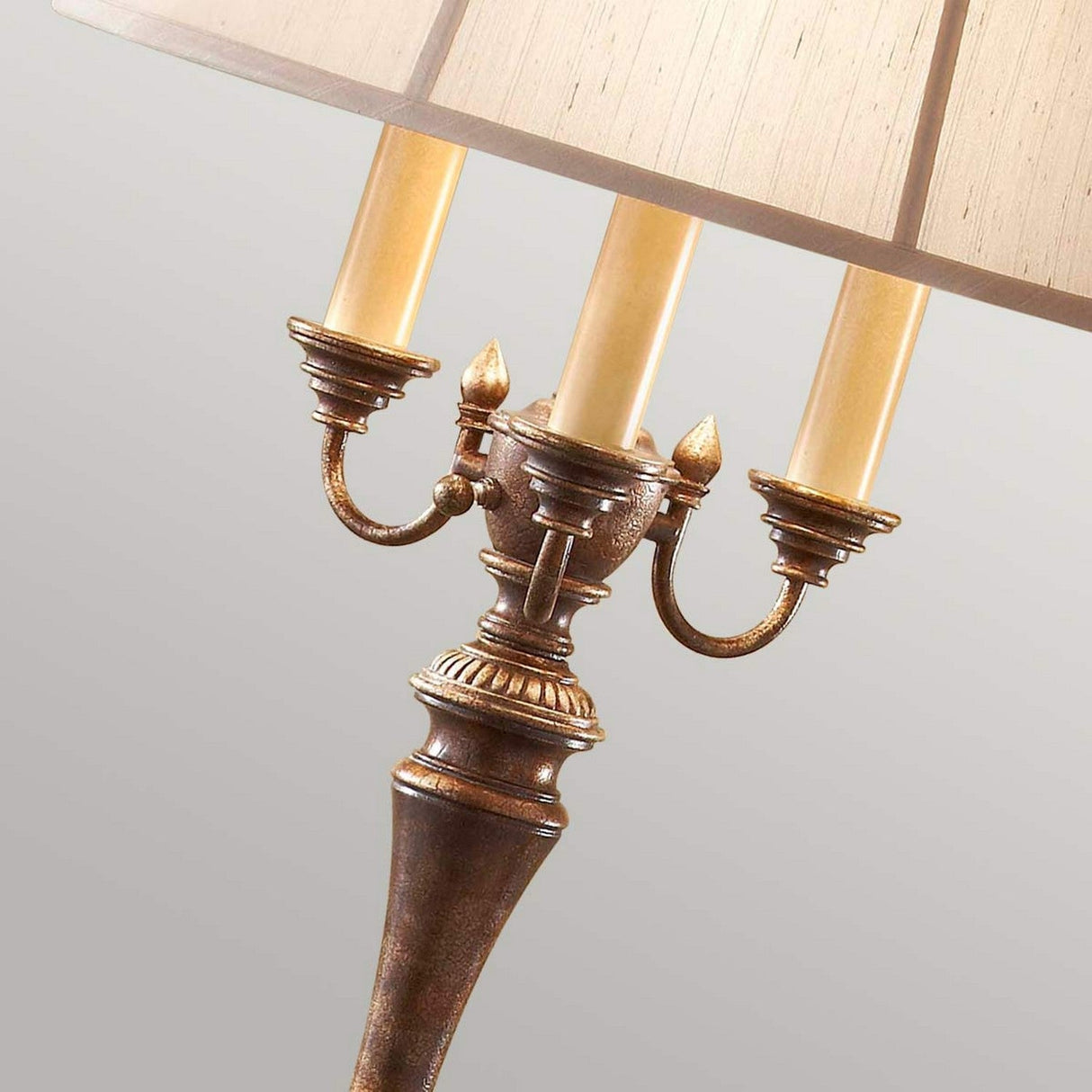 Introducing the Gibson 4 Light Floor Lamp in Dark Brown—a vintage-inspired lighting piece that features an ornate metallic base with three candle-like light fixtures. Its large beige lampshade emits a warm, inviting glow, perfect for adding timeless elegance to any space.