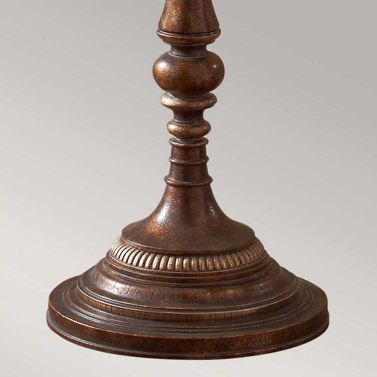 Close-up of an ornate bronzed metal stand or lamp base with intricate carvings, exuding a vintage lighting design. This Gibson 4 Light Floor Lamp - Dark Brown features a circular design on a light gray background, perfect for creating an ambient atmosphere.