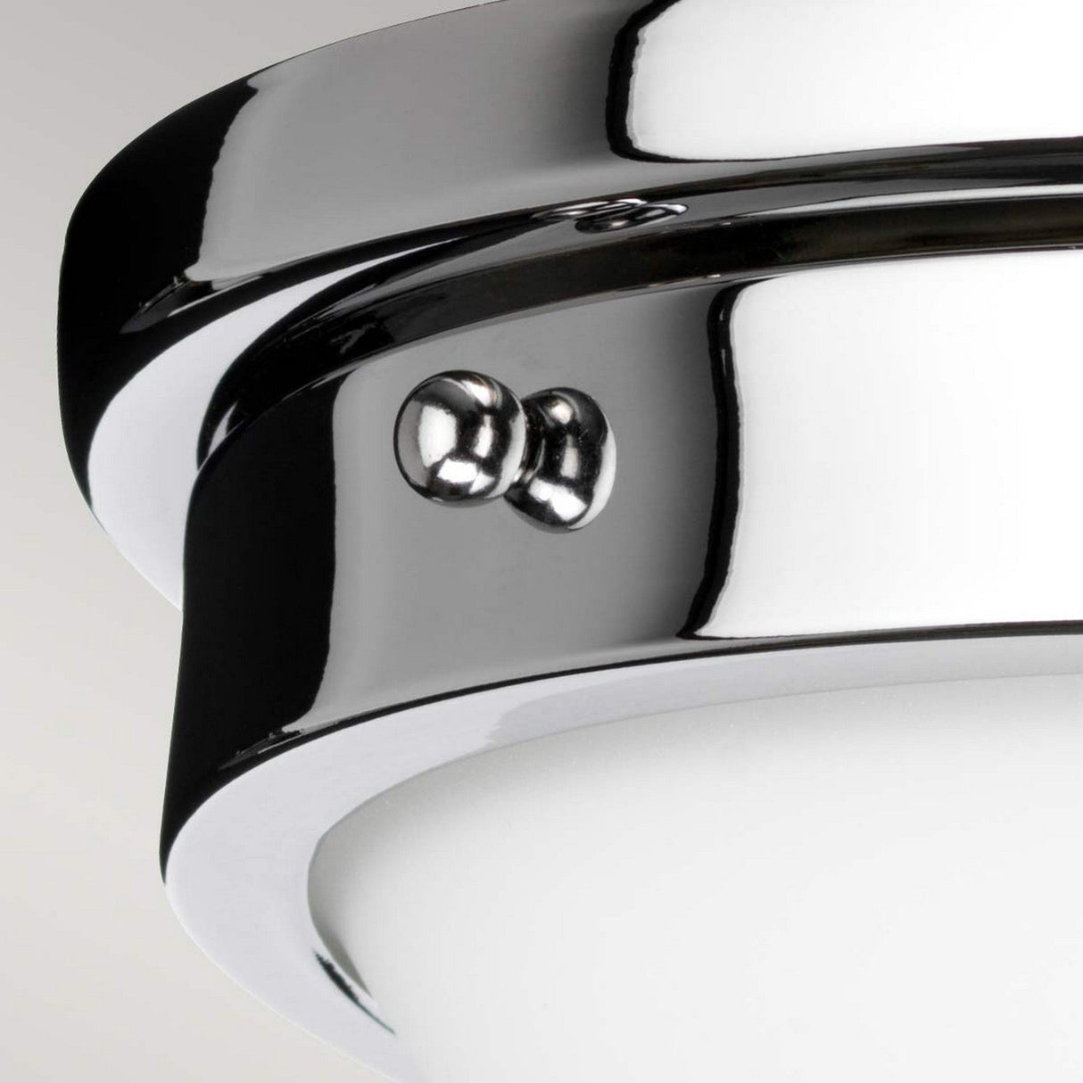 Close-up of the Gravity 2 Light Flush - Polished Chrome, a contemporary lighting piece with smooth, curved surfaces and two metallic screws securing the fixture, set against a plain, neutral background.