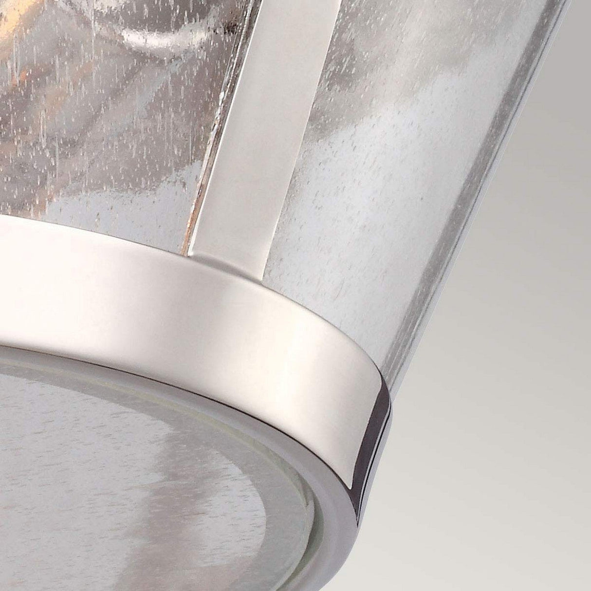 Close-up of a modern light fixture with a clear seeded glass shade and a polished nickel rim. The visible hints of the bulb and electrical components inside add an element of intrigue. This contemporary Harrow 2 Light Flush - Polished Nickel design is set against a neutral background, exuding elegance and sophistication.