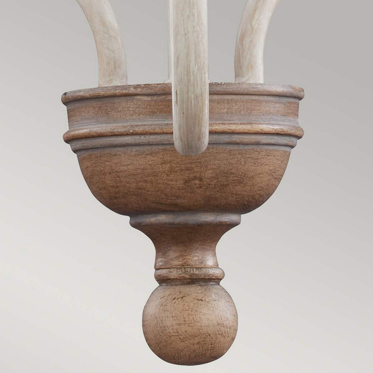 Close-up of the Hartsville 3 Light Chandelier in a Chalk Washed/Beachwood finish, showcasing a wooden finial with a smooth, rounded shape, ideal for rustic design. The layered detailing is attached to curving wooden elements above, resembling those in coastal casual spaces. A neutral gray backdrop enhances its understated elegance.