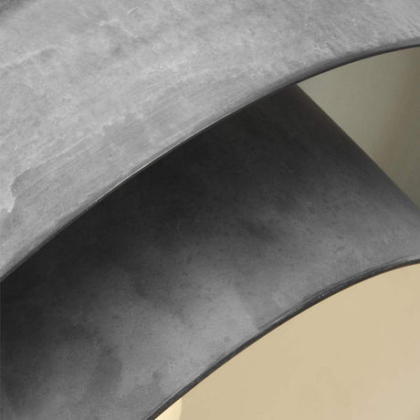 Close-up of the Haymarket 1 Light Pendant - Weathered Galvanized, showcasing its modern design with smooth, curved gray surfaces. This product features two overlapping arcs that form a layered effect against a light, neutral background, exuding an industrial aesthetic and complementing its sleek form.