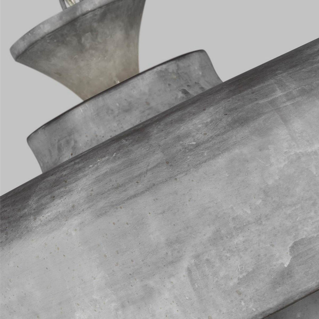 Close-up of the Haymarket 1 Light Pendant - Weathered Galvanized with overlapping cylindrical shapes and a speckled texture, evoking an industrial aesthetic, set against a plain light gray background.