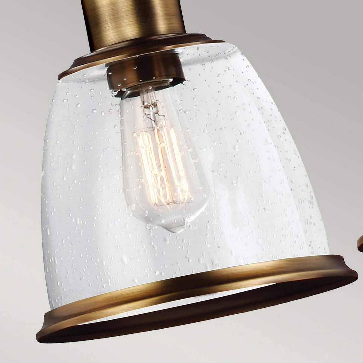 A close-up of the Hobson 3 Light Island Light in aged brass features a clear, seeded glass shade that encases an Edison-style bulb. The bubbled effect in the glass enhances its vintage appeal, making it an ideal choice for an elegant island light arrangement.