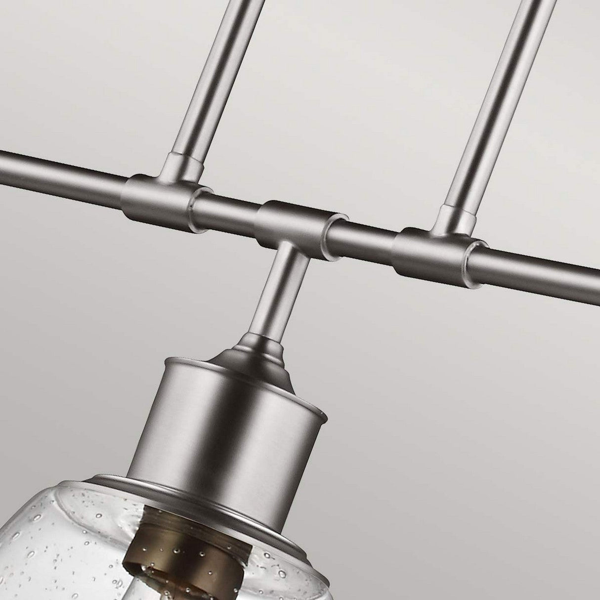 Close-up of the Hobson 3 Light Island Light in a modern satin nickel finish, featuring a cylindrical design. This light fixture is connected to rods and supports a clear seeded glass dome, partially exposing the bulb inside. Set against a plain light gray background, it emphasizes its industrial design aesthetic.