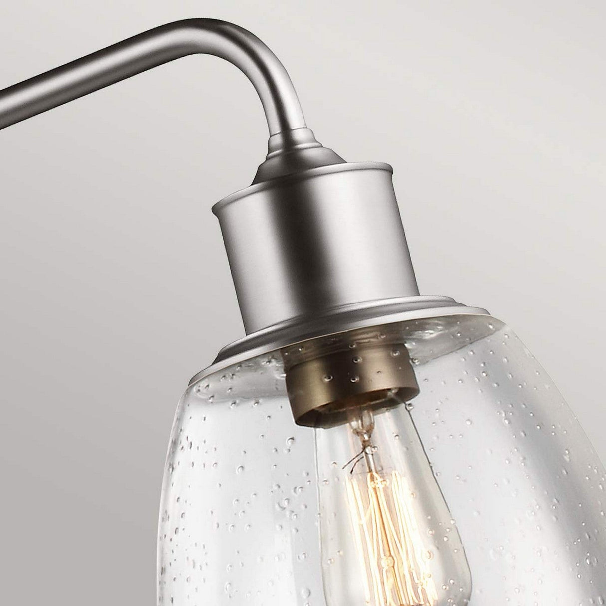Close-up of the Hobson 3 Light Island Light in satin nickel, featuring a curved arm and clear seeded glass shade, highlighting a vintage-style filament bulb within. The textured, bubble-like appearance of the glass enhances the industrial design element.