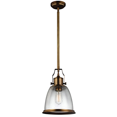 The Hobson 1 Light Medium Pendant - Aged Brass showcases an aged brass finish and a clear glass bell-shaped shade. It suspends from a lengthy brass rod, complemented by a visible Edison bulb that accentuates its industrial charm.