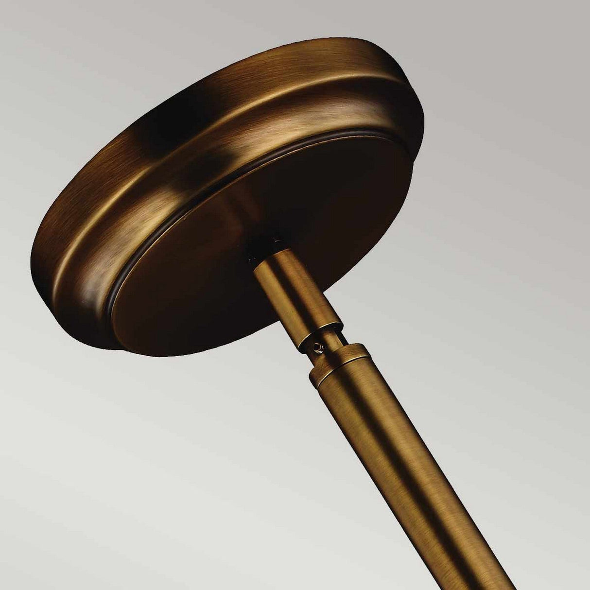 Close-up of the Hobson 1 Light Medium Pendant in an aged brass finish, showcasing its round ceiling plate and rod attachment against a gray backdrop. This fixture radiates elegance and charm, making it an ideal centerpiece for any room.