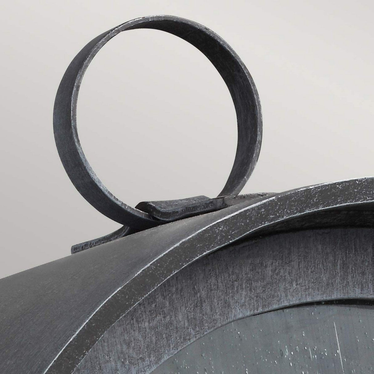 Close-up of the top of a vintage-style Hodges Outdoor Small Wall Lantern in ash black with a round handle. The surface is slightly weathered, giving it an antique look reminiscent of prairie design. The background is a neutral gray color.