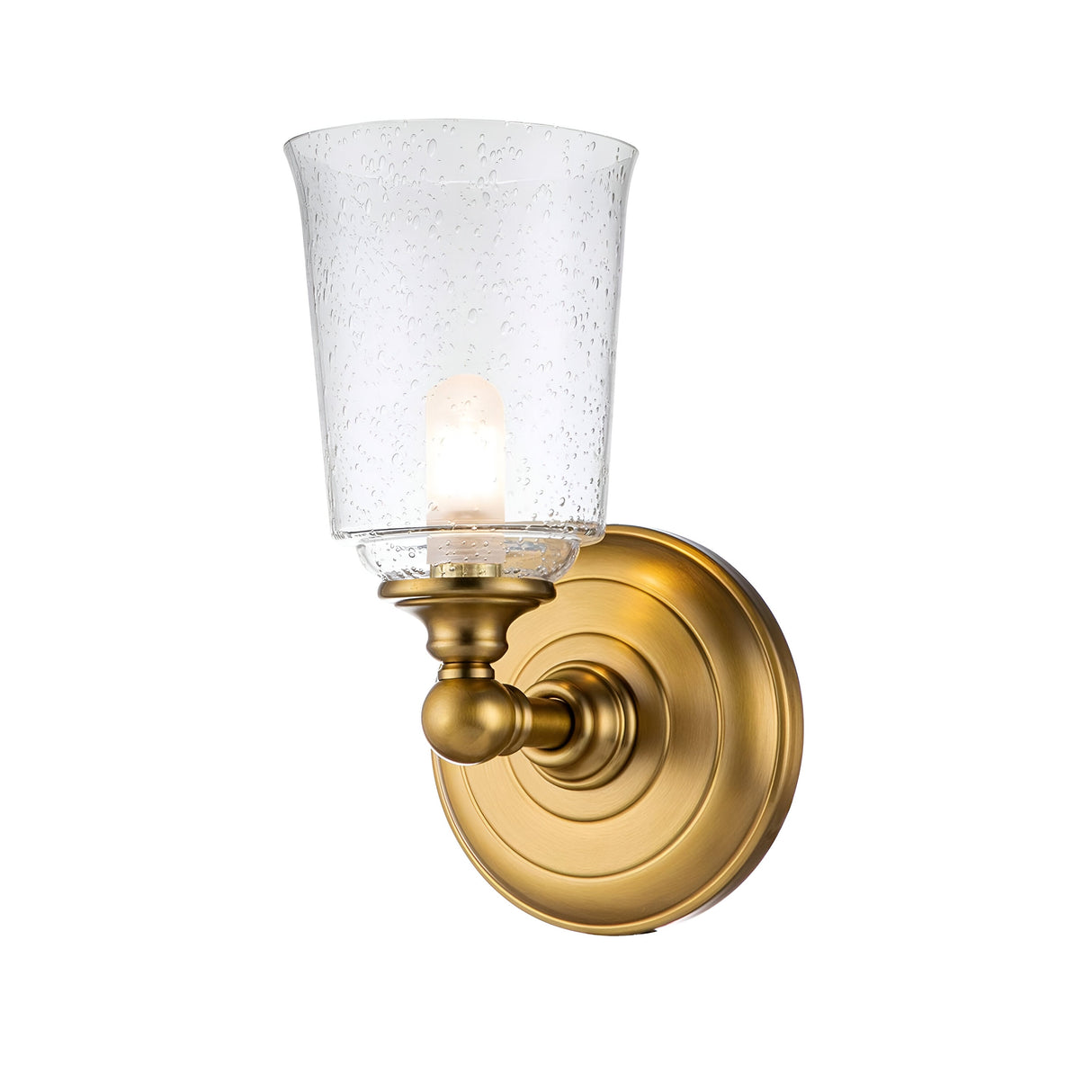 The Huguenot Lake 1 Light Wall Light in burnished brass combines a refined base with an elegant seeded glass shade. The subtly textured glass encases a visible bulb, providing a gentle glow and delivering a timeless and sophisticated style.