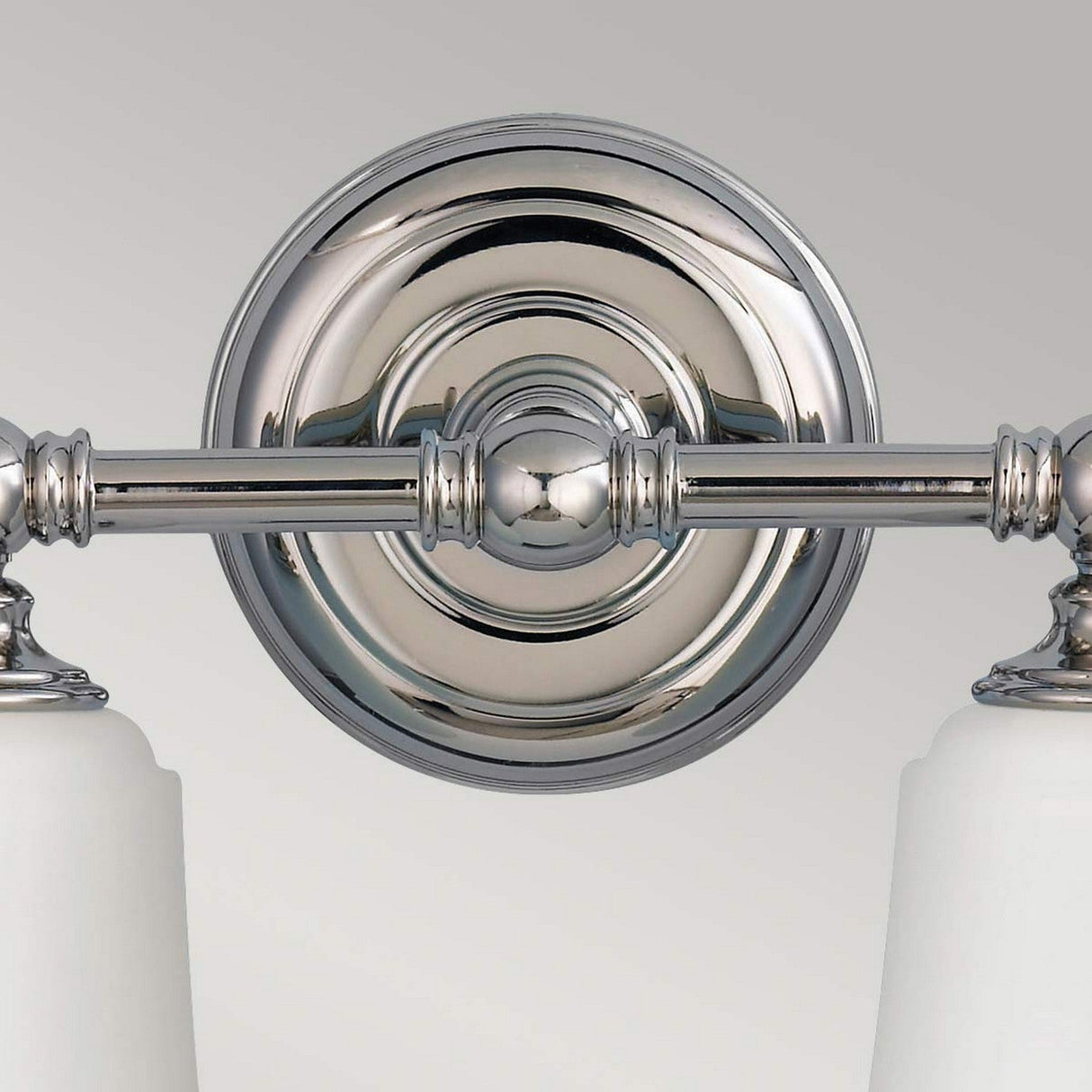 Close-up of the Huguenot Lake 2 Light Wall Light in polished chrome, featuring a circular wall mount and two seeded glass shades extending downward. The reflective surface showcases a clean, modern design, ideal for elegant bathroom lighting against a neutral background.