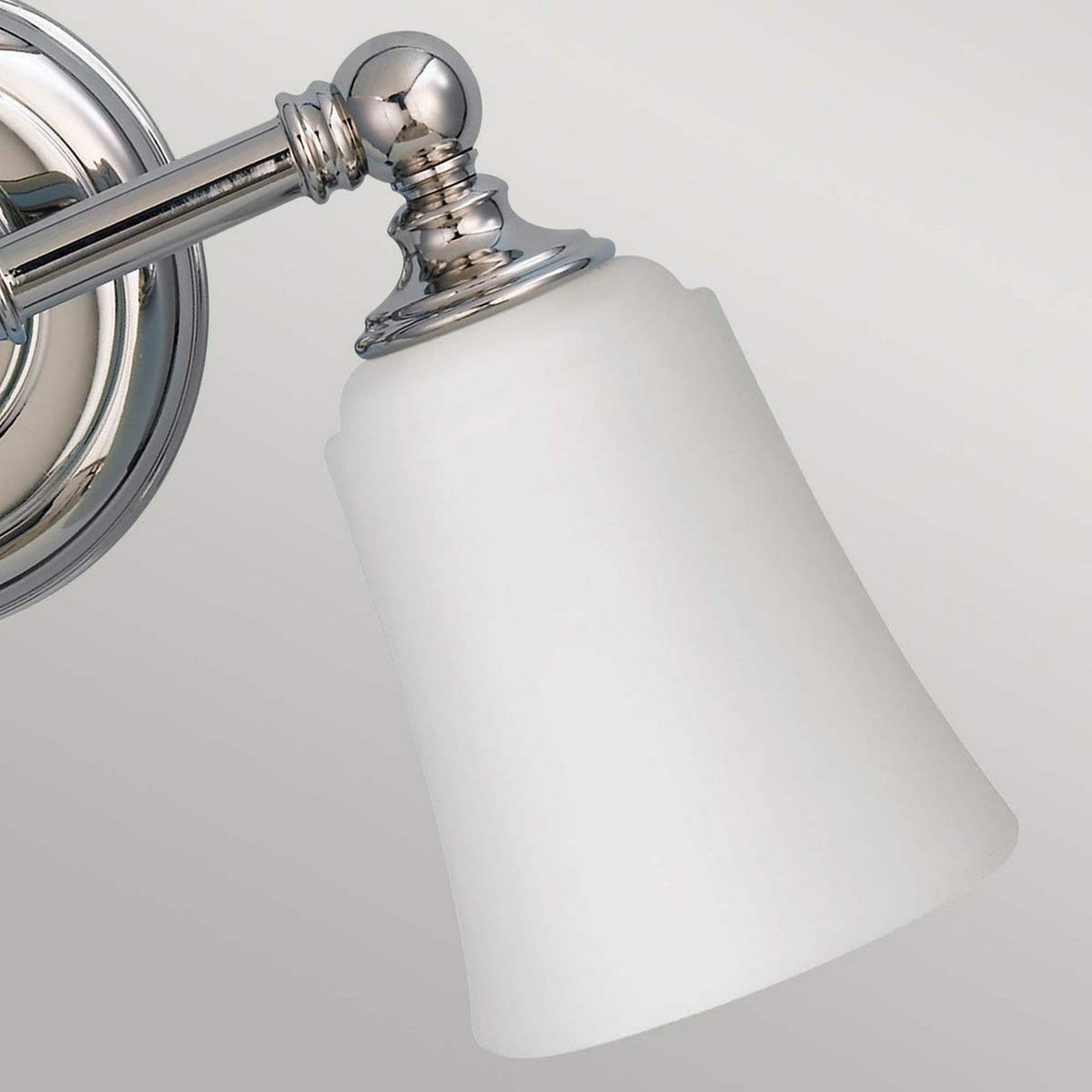 The Huguenot Lake 2 Light Wall Light, with its metallic base in a polished chrome finish and bell-shaped frosted glass shade, is ideal for bathroom lighting. This fixture is designed to mount angled slightly downward against a plain background.