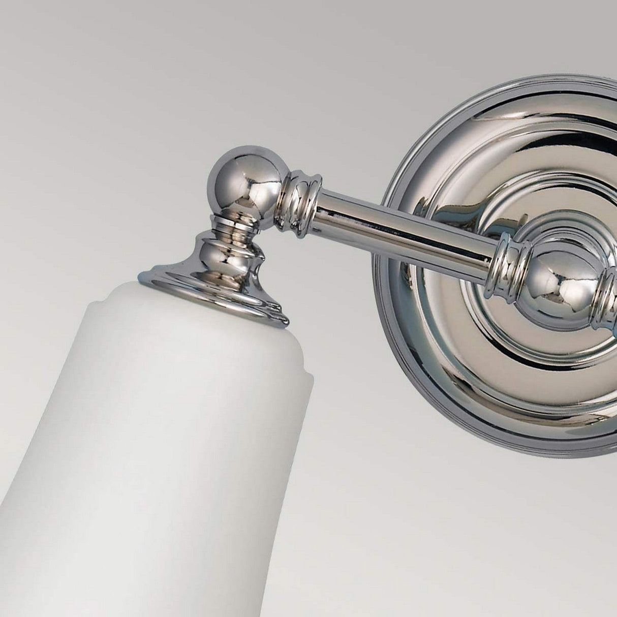 Close-up of the Huguenot Lake 2 Light Wall Light in polished chrome, featuring a frosted white glass shade. Ideal for bathroom lighting, this classic design includes a round base and decorative arm, set against a neutral background.