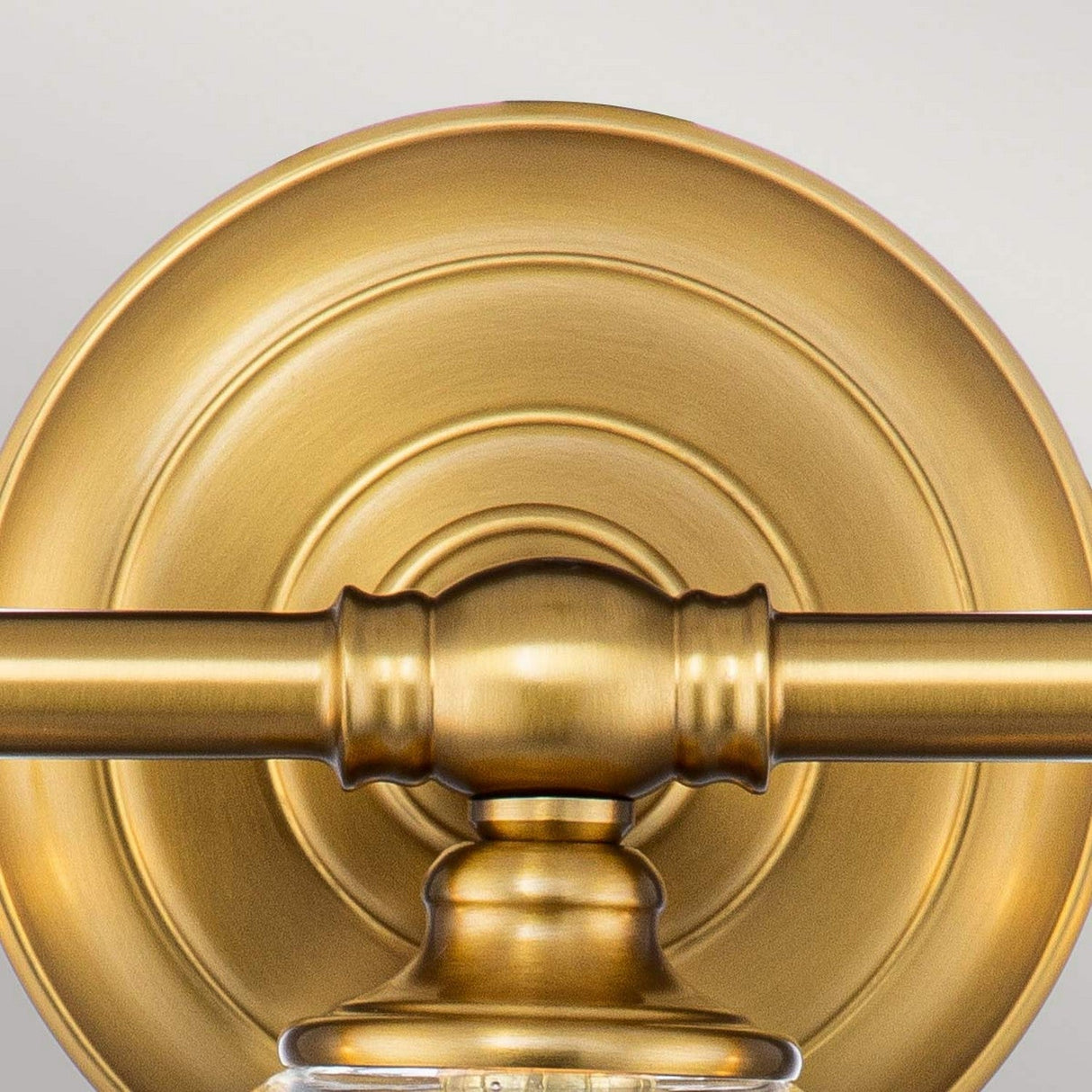 Close-up of the Huguenot Lake 3 Light Wall Light in a gold, circular form with intricate detailing. This burnished brass fixture showcases a colonial design with a central rod and warm metallic finish, exuding timeless elegance.