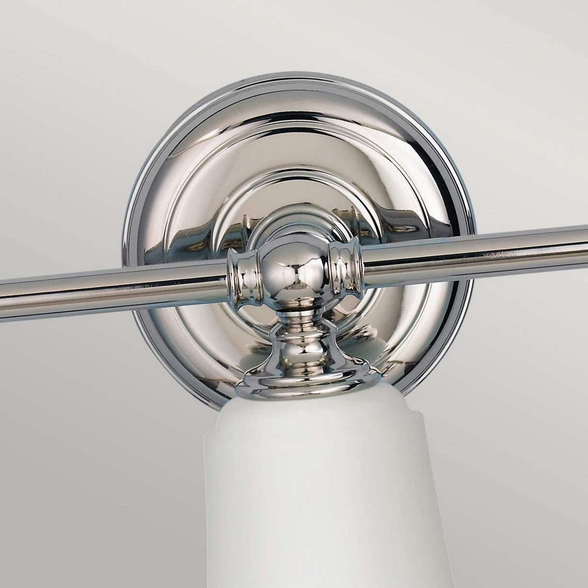 A close-up of the Huguenot Lake 3 Light Wall Light - Polished Chrome highlights its elegant design with a polished circular backplate and horizontal rod. It boasts a white conical glass shade, offering a modern and sleek look that epitomizes contemporary style.