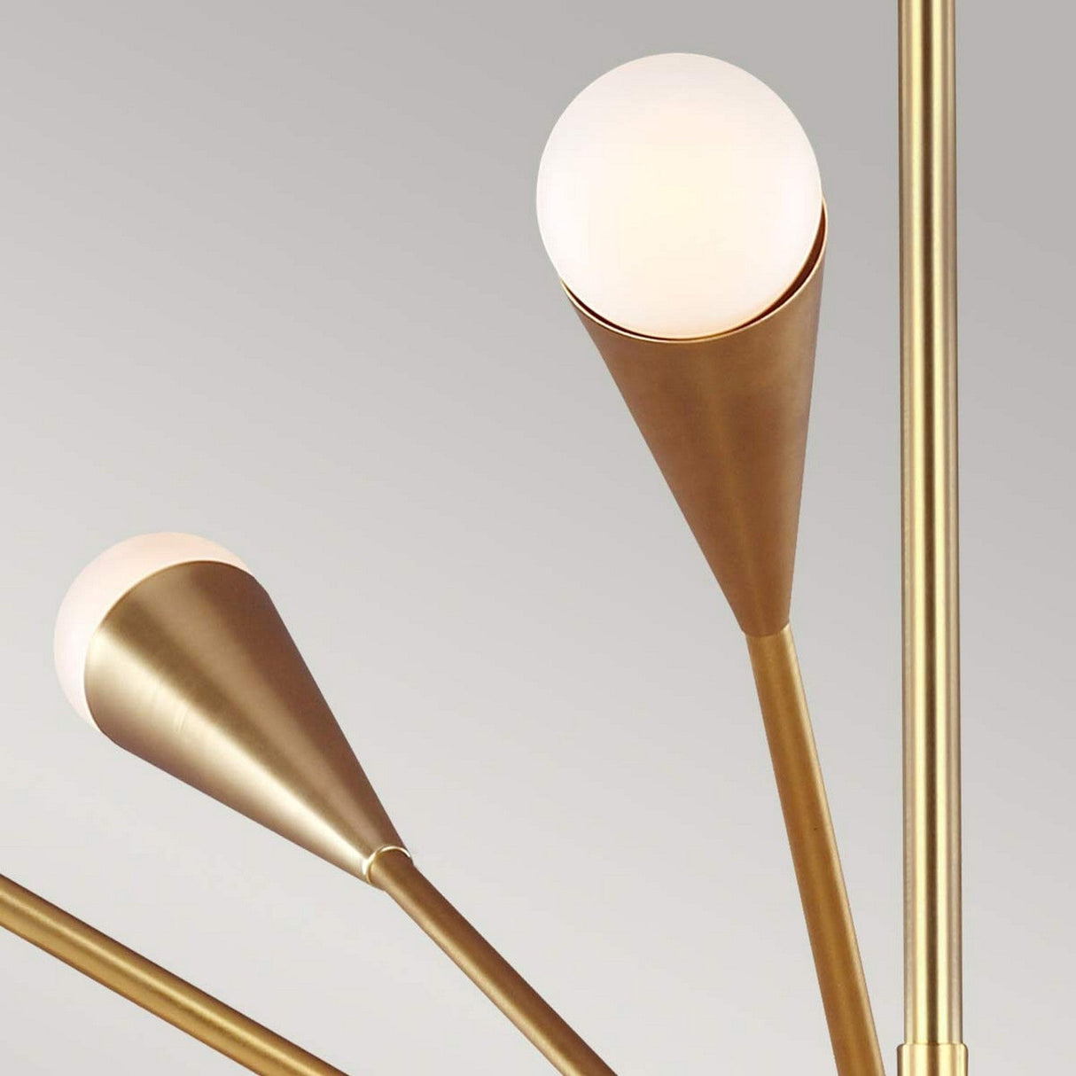 Close-up of the Jax 10 Light Chandelier - Burnished Brass displaying a minimalist Art Deco design with burnished brass rods and cone-shaped lamp holders. Each holder contains a frosted glass globe bulb, beautifully positioned against a neutral gray background.