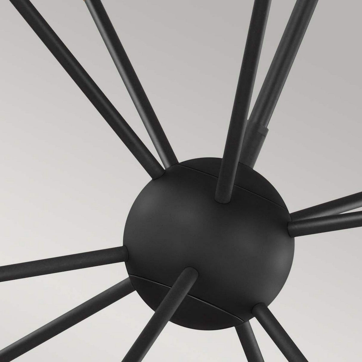 Close-up of the Jax 10 Light Chandelier in Midnight Black, featuring a central spherical hub with multiple rods extending outward in a radial pattern, resembling a modern sculpture or molecular structure, set against a light gray background.
