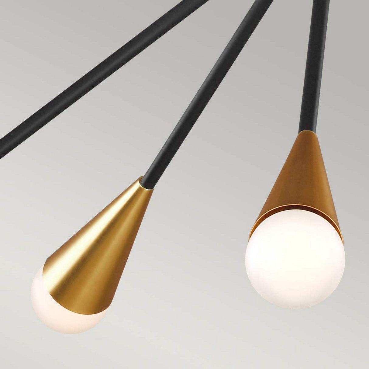 The Jax 10 Light Chandelier in Midnight Black showcases a modern geometric design, featuring two cone-shaped pendant lights. With gold cones and matte black stems, it holds spherical white bulbs that emit a soft glow against the light gray background, embodying an Art Deco lighting flair.