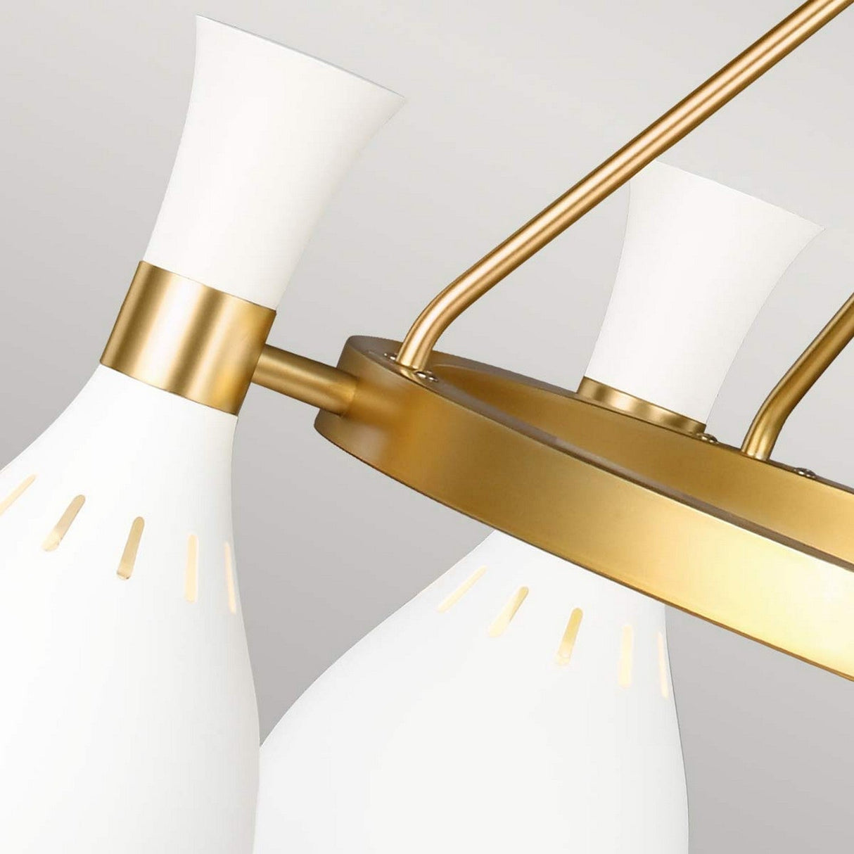 Close-up of the Joan 5 Light Chandelier, showcasing modern elegance with its matte white cone-shaped lampshades and burnished brass finish. The sleek design features a circular frame supporting the shades, offering a stylish and sophisticated appearance.