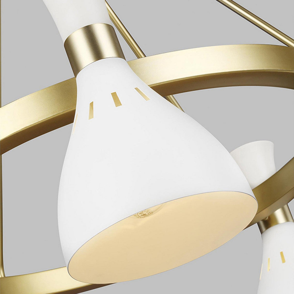 Close-up of the Joan 5 Light Chandelier, showcasing its modern design with a matte white cone-shaped shade and elegant burnished brass details. Intersecting gold rings in the background enhance its minimalist chandelier aesthetic.