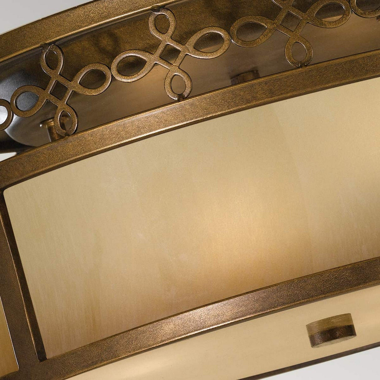 Close-up view of the Justine 3 Light Flush in Astral Bronze, featuring handcrafted iron detailing with decorative loop patterns and frosted glass, emitting a warm glow that encapsulates rustic elegance.