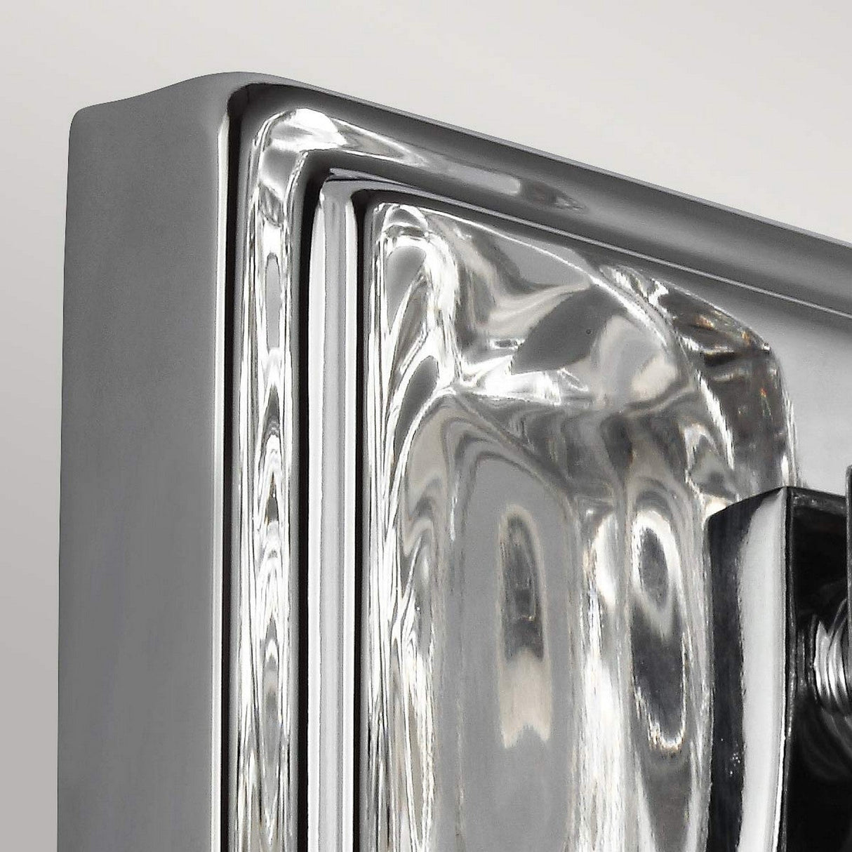 A close-up of a polished chrome object with geometric lines and reflective surfaces, reminiscent of the Kalli 1 Light Wall Light - Polished Chrome, is set against a light gray background.