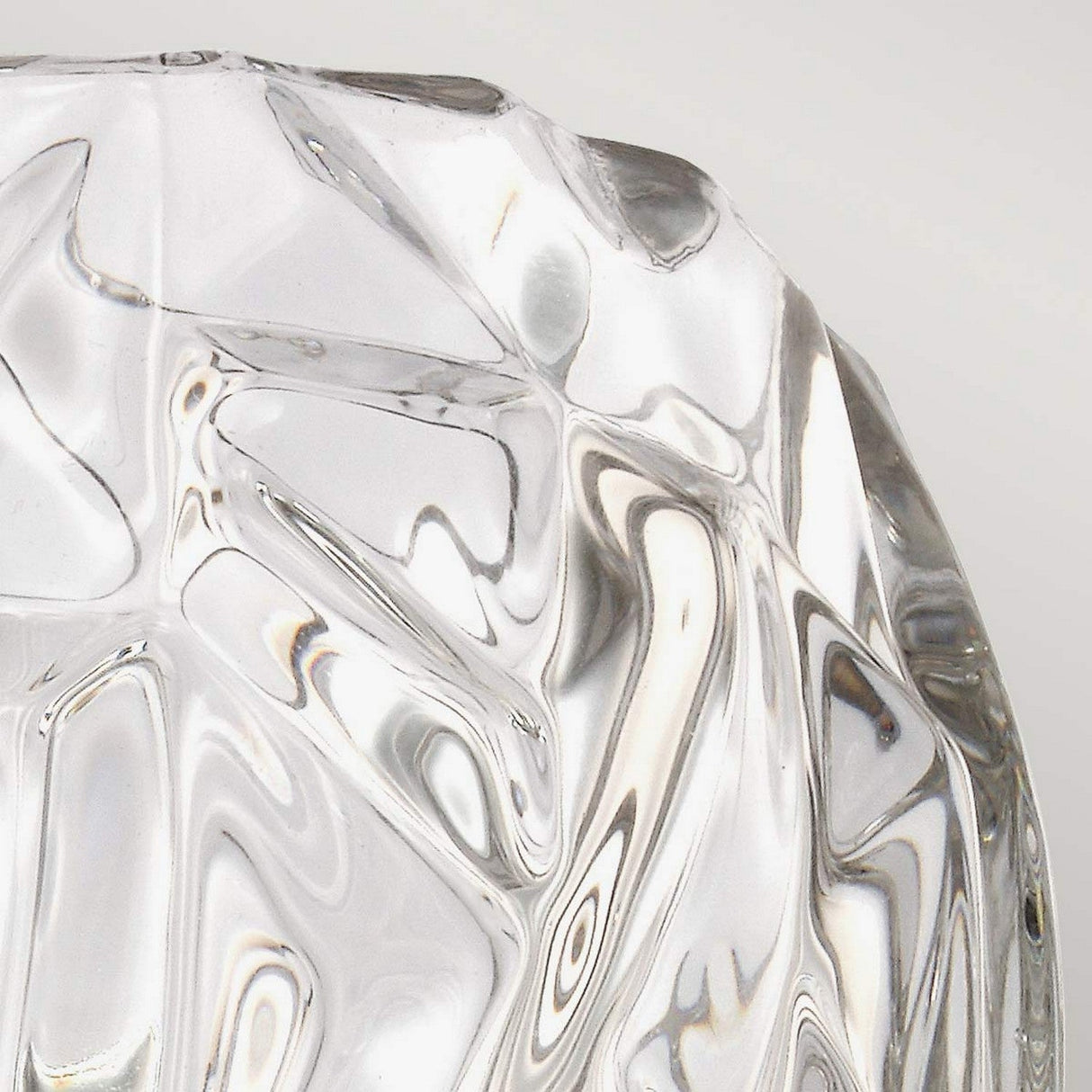 Close-up of a textured, clear glass surface with faceted patterns producing a prismatic effect similar to the crystal glass shades of the Kalli 1 Light Wall Light - Polished Chrome. The light reflects and refracts through the polished chrome features, creating a visually intricate and abstract appearance.