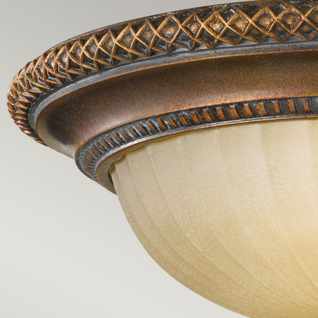 A detailed view of the Kelham Hall 2 Light Flush showcases an ornate rim in British bronze paired with a frosted glass shade. The rim displays intricate patterns inspired by Kelham Hall, while the gracefully curved glass imbues the fixture with elegance.
