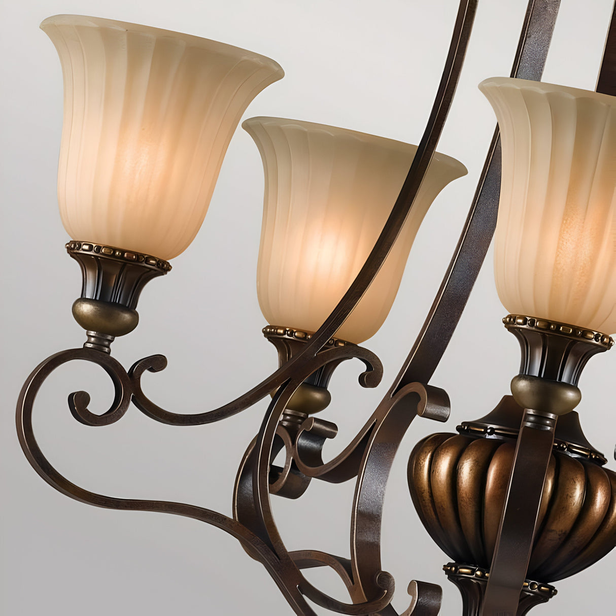 A detailed view of the Kelham Hall 5 Light Up Light Chandelier, showcasing three frosted glass lampshades. The intricate metal framework features graceful, curved patterns and a refined British Bronze finish, radiating a warm and welcoming light.