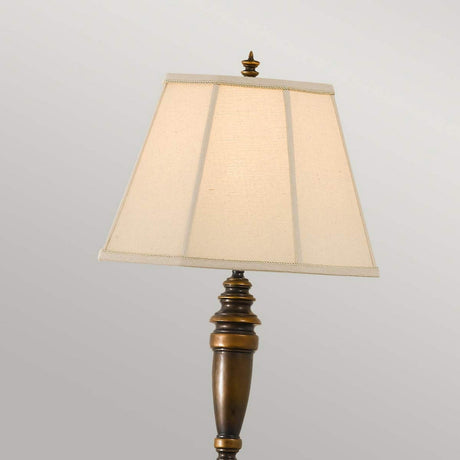 The Lincolndale 1 Light Floor Lamp in astral bronze, with its tall and elegant design, showcases a beige linen shade against a light gray background.