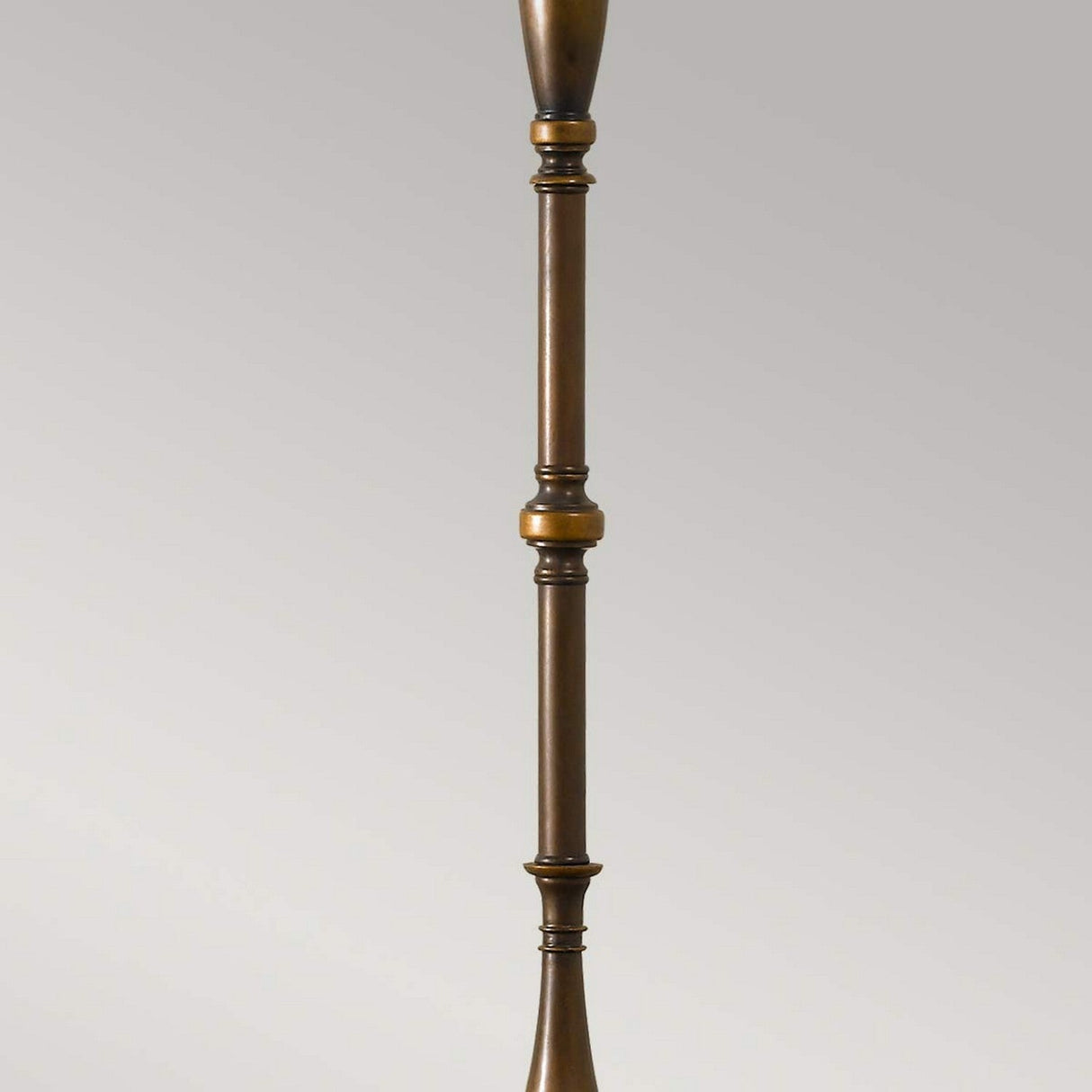The Lincolndale 1 Light Floor Lamp in Astral Bronze features a tall, slender design with intricate detailing set against a plain background. It includes turned sections and a central spherical element, all elegantly complemented by a sophisticated linen shade.