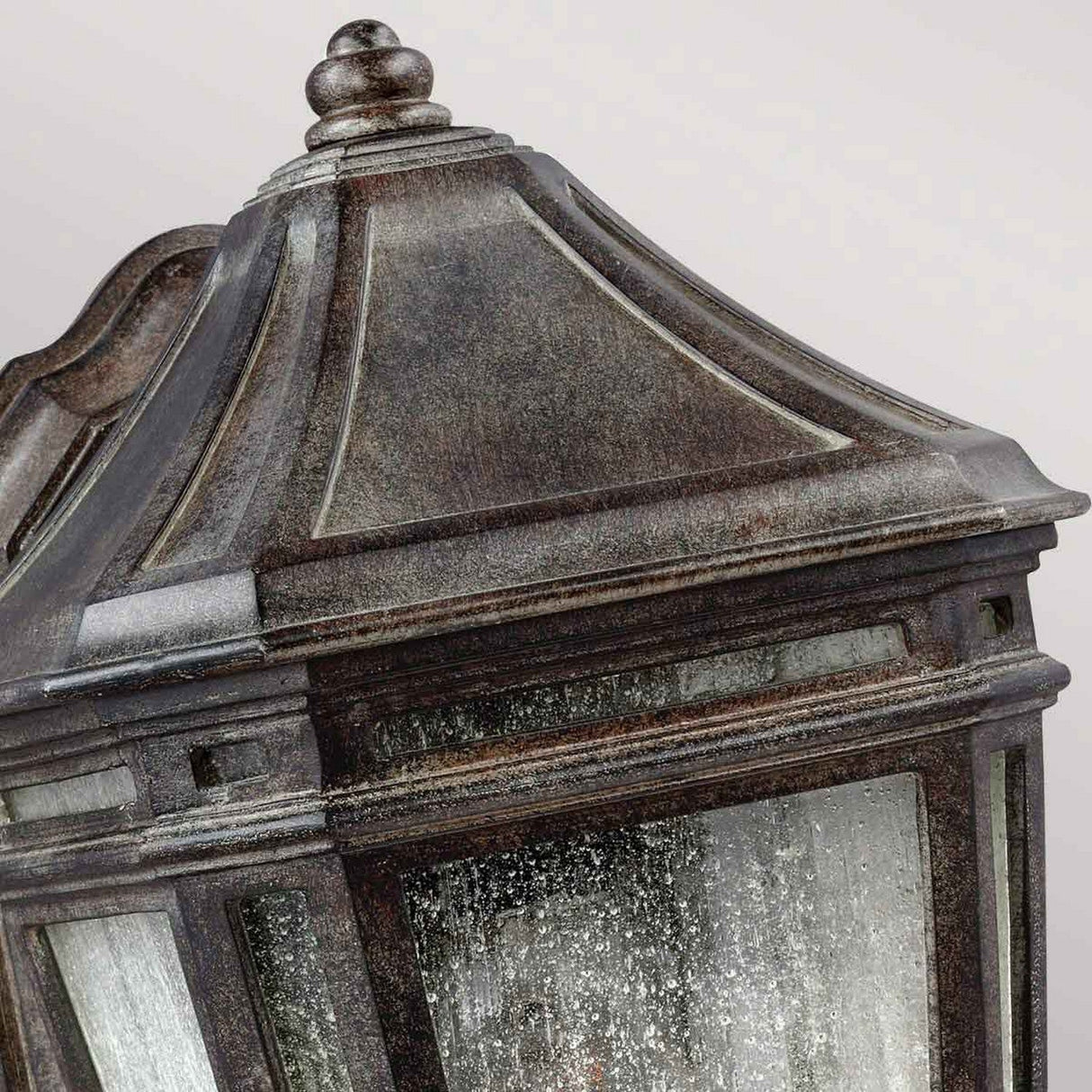 Close-up of the Londontowne 1 Light Outdoor Wall Lantern in Weathered Chestnut finish, showcasing a vintage-style design with a decorative angular top and seeded glass panels that evoke an antique look.