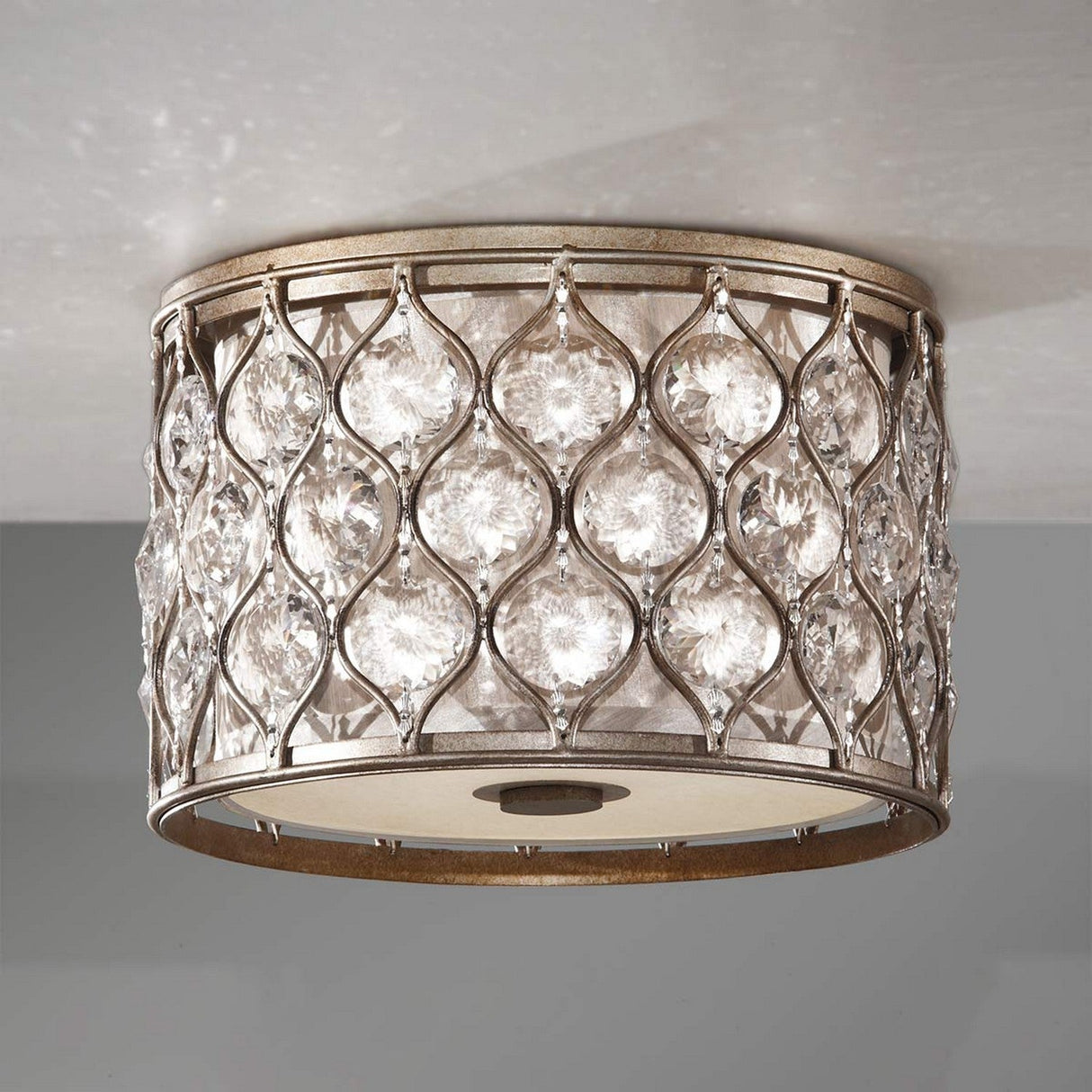 Introducing the Lucia 2 Light Flush in Burnished Silver, a stunning decorative ceiling fixture featuring a round metallic frame adorned with an intricate diamond pattern. This exquisite design houses multiple large, clear Bauhinia crystals, casting an elegant and shimmering effect against a light gray ceiling.