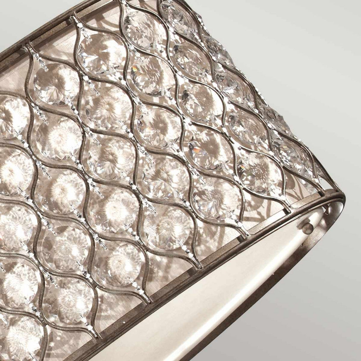 A close-up of a decorative lamp shade in burnished silver showcases a metal lattice design accented with Bauhinia crystals. These features produce a sparkling effect, set against a white background to emphasize the intricate details, similar to those found in the Lucia 3 Light Large Chandelier - Burnished Silver.