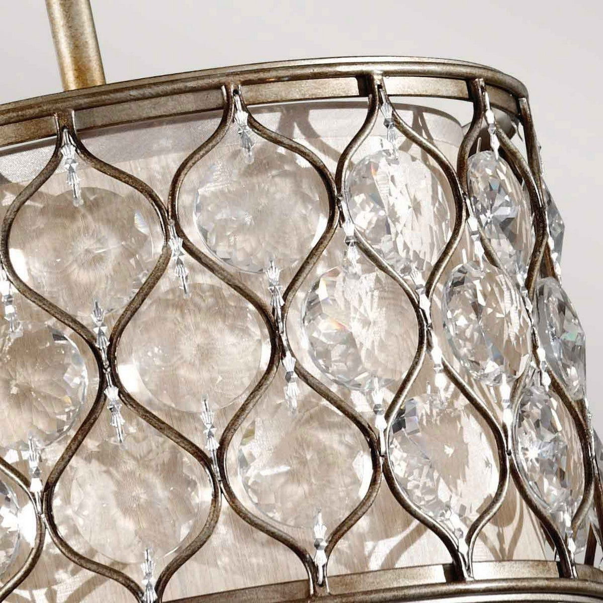 A close-up of the Lucia 1 Light Pendant Light reveals a metal frame featuring an intricate lattice design. Nestled within the gaps are multiple clear Bauhinia crystals that capture and reflect light, producing a sparkling effect reminiscent of burnished silver.