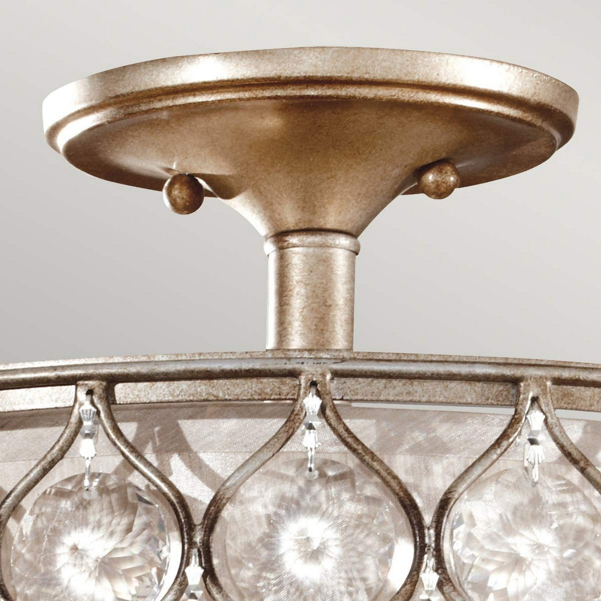 Close-up of the Lucia 1 Light Semi Flush with an elaborate burnished silver finish and Bauhinia Crystals. The fixture showcases a circular design adorned with clear, round crystal accents suspended in a pattern around the frame, beautifully reflecting light. The backdrop is a plain, light-colored wall.