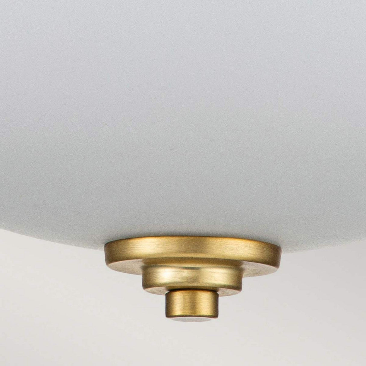 A detailed view of the Malibu 2 Light Flush - Brushed Brass fixture showcases a modern aesthetic with its opal-etched glass drum shade and sophisticated brushed brass accents, accentuated by concentric circular designs.