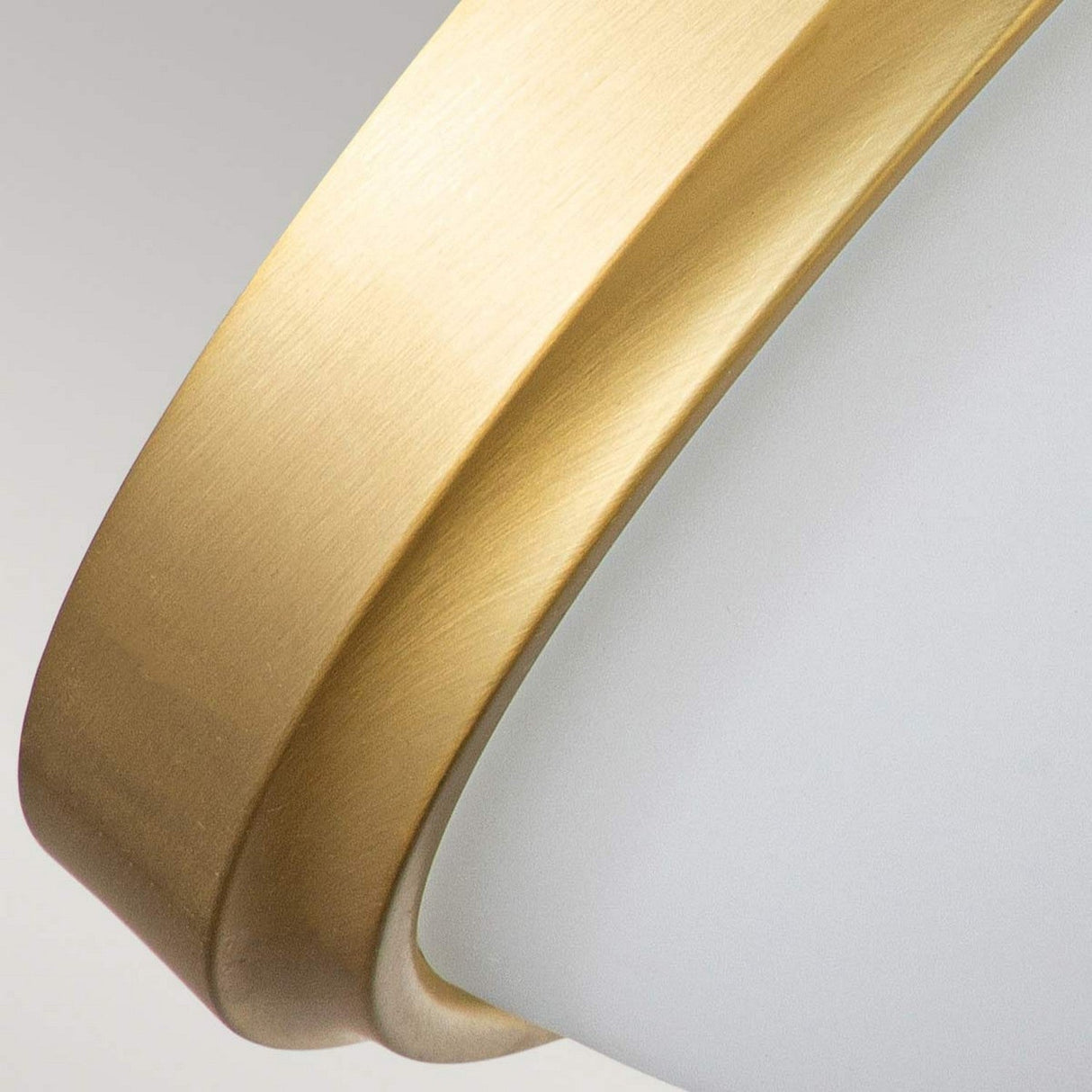 A close-up of the Malibu 2 Light Flush - Brushed Brass showcases its modern design with a curved, brushed brass frame and an opal-etched glass drum shade. This sleek fixture emphasizes the textural contrast between the shining brass and matte surfaces, delivering a minimalist aesthetic.