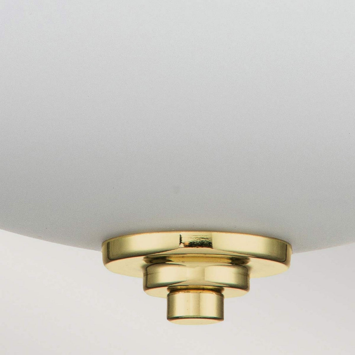 The Malibu 2 Light Flush in Polished Brass features a close-up of its white lampshade complemented by a gold metallic fixture at the bottom. Its polished brass construction enhances the minimalist design with elegance, and when lit, ambient lighting accentuates the smooth texture, casting a warm glow.