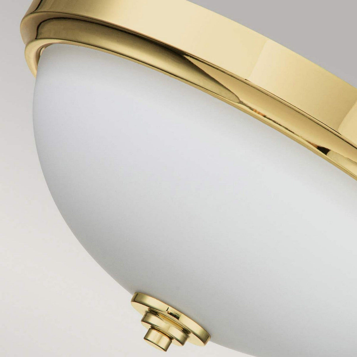 A close-up of the Malibu 2 Light Flush in polished brass showcases its elegant detailing, featuring a smooth and reflective rim that contrasts with the matte surface of the opal-etched glass dome. This fixture provides soft ambient lighting through its decorative knob at the bottom.