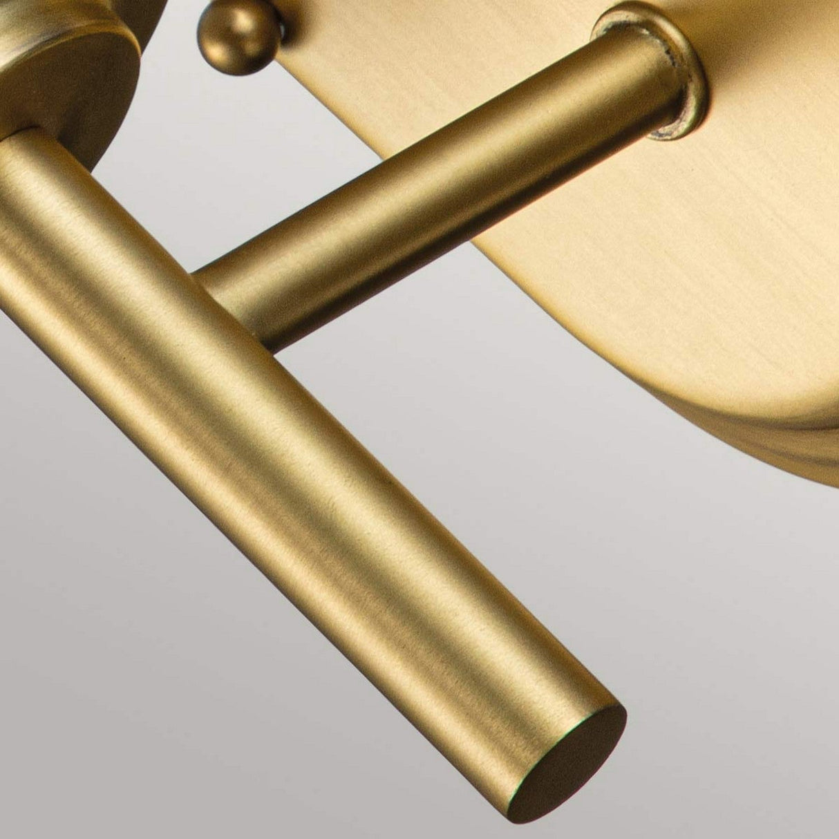 A close-up of a modern, brass-colored metal structure mirrors the sleek design of the Malibu 1 Light Wall Light in brushed brass. Cylindrical rods intersect at right angles, highlighting the brushed metallic finish and minimalist aesthetic against a neutral backdrop.