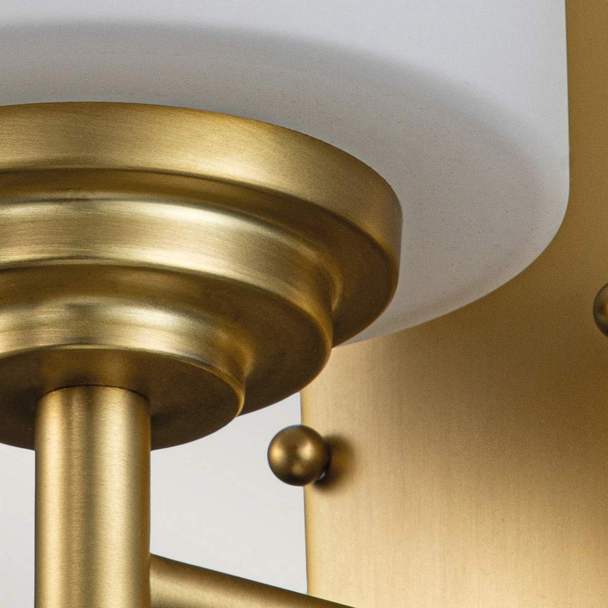 Close-up of the Malibu 1 Light Wall Light in brushed brass featuring an opal-etched glass shade. The design presents cylindrical elements and a metallic finish, effortlessly merging modern and classic aesthetics while offering IP44-rated durability.