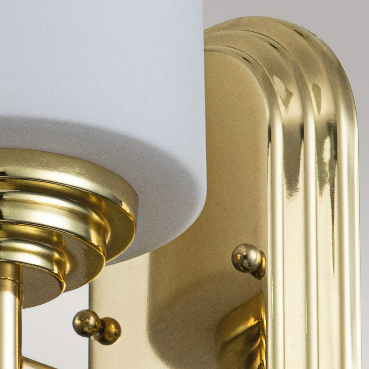 Close-up of the Malibu 1 Light Wall Light in polished brass, showcasing a sleek, curved design. The fixture highlights a white cylindrical lampshade at the top, complemented by shiny gold-toned metal and attached to an opal-etched glass backplate.