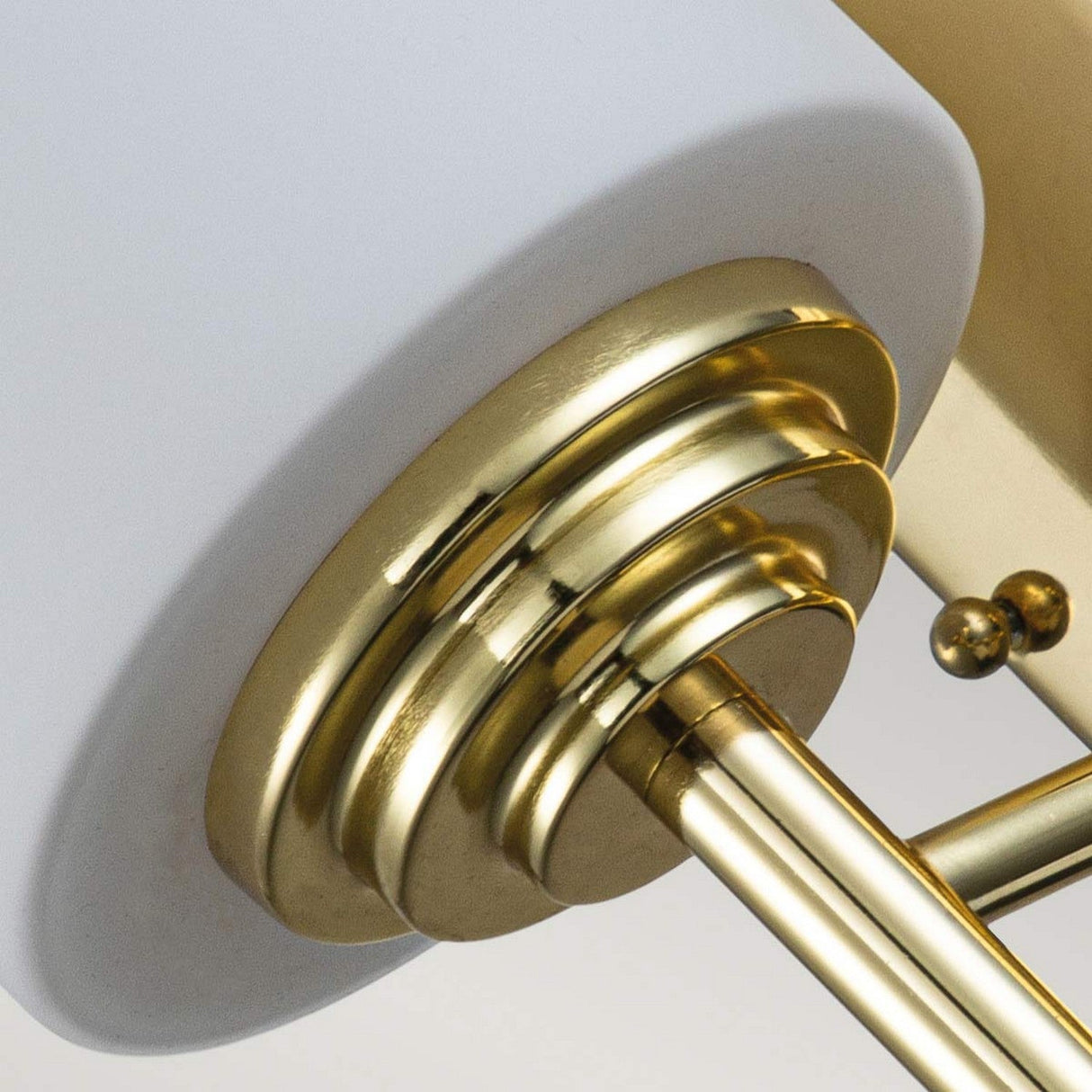 Close-up of the Malibu 1 Light Wall Light, featuring a modern design with a white cylindrical shade and polished brass accents. This fixture highlights its sleek and contemporary style with a shiny gold rod and decorative knob.